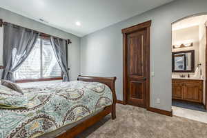 Bedroom with light colored carpet, arched walkways, connected bathroom, and recessed lighting
