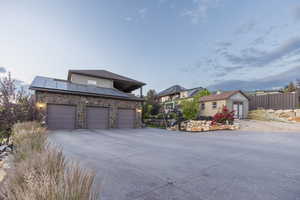 Contemporary house featuring roof mounted solar panels, an outbuilding, stone siding, concrete driveway, and an attached garage