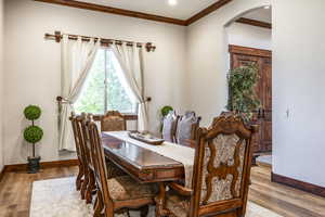 Dining room with arched walkways, crown molding, and wood finished floors