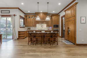 Kitchen with stainless steel oven, ornamental molding, black microwave, a kitchen island, and light wood finished floors