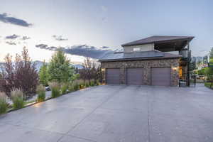 View of property exterior featuring stairs, a standing seam roof, solar panels, driveway, and stone siding