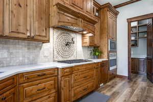 Kitchen with appliances with stainless steel finishes, brown cabinetry, dark wood-type flooring, light countertops, and ornamental molding