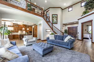 Living room with arched walkways, light wood finished floors, stairway, a towering ceiling, and ornamental molding