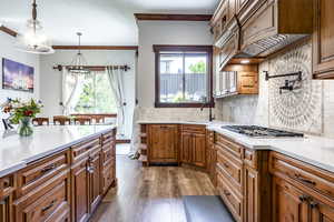 Kitchen featuring wood finished floors, light countertops, stainless steel gas cooktop, brown cabinetry, and backsplash