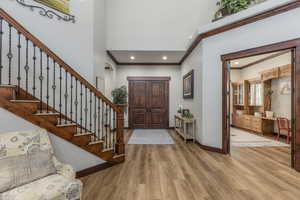 Foyer entrance with ornamental molding, wood finished floors, stairs, a high ceiling, and recessed lighting