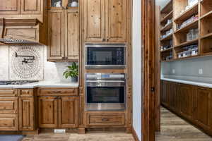 Kitchen featuring stainless steel appliances, light wood finished floors, light countertops, backsplash, and brown cabinets