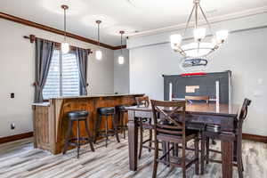 Dining room featuring light wood-style flooring, a bar, and crown molding