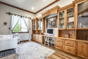 Office area with built in study area, crown molding, and light wood-style flooring