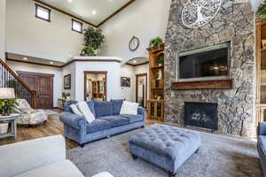Living area with crown molding, high vaulted ceiling, a fireplace, stairway, and wood finished floors