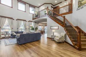 Living room featuring a high ceiling, arched walkways, stairs, crown molding, and light wood-style flooring