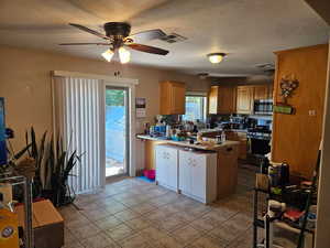 Kitchen featuring stainless steel appliances, a peninsula, a ceiling fan, plenty of natural light, and a textured ceiling