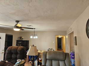 Living area featuring a ceiling fan, a textured ceiling, and a chandelier