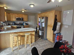 Kitchen featuring a peninsula, stainless steel appliances, a kitchen bar, light tile patterned flooring, and ceiling fan