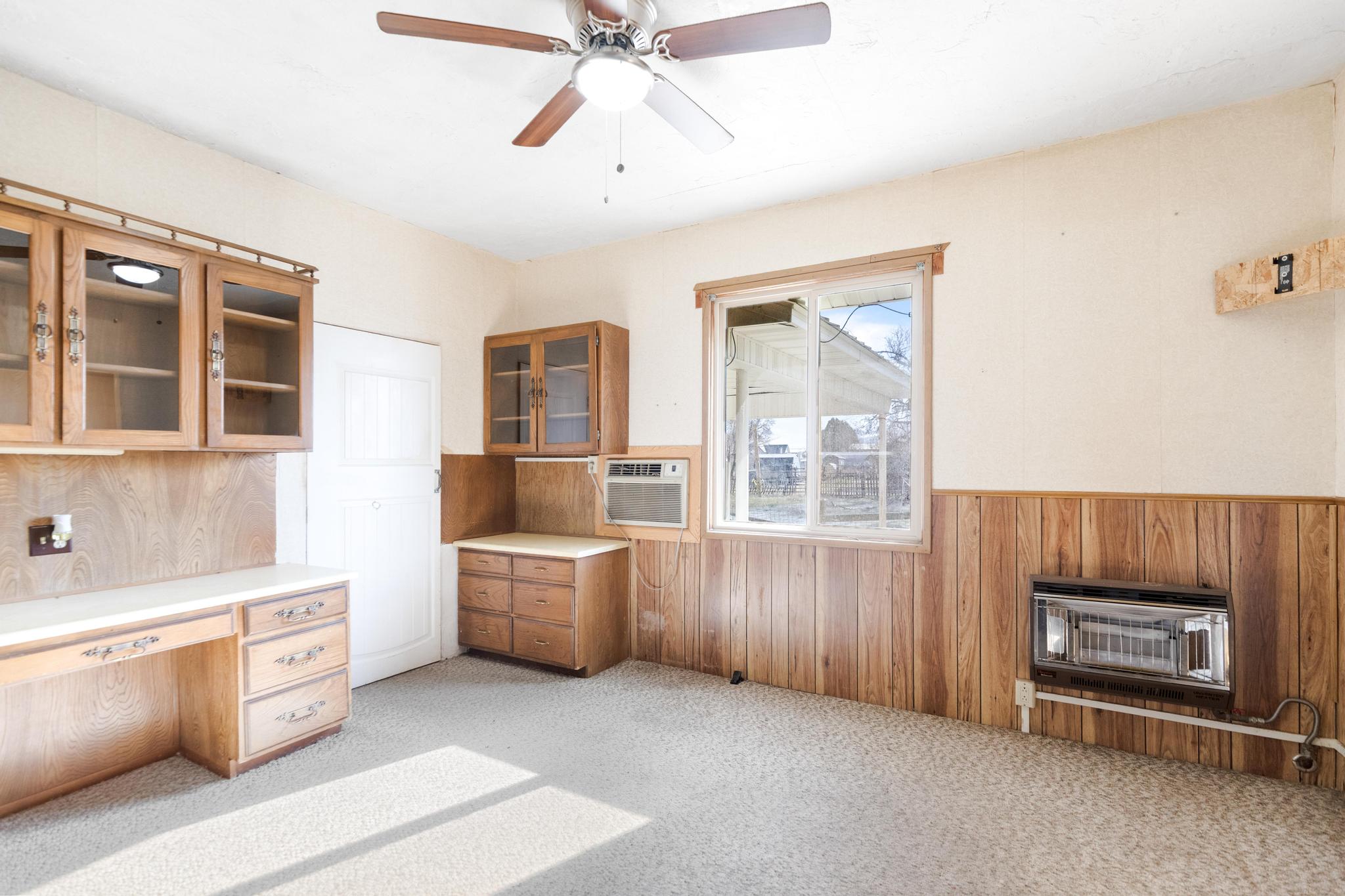 Unfurnished office with wooden walls, heating unit, a ceiling fan, light carpet, and wainscoting