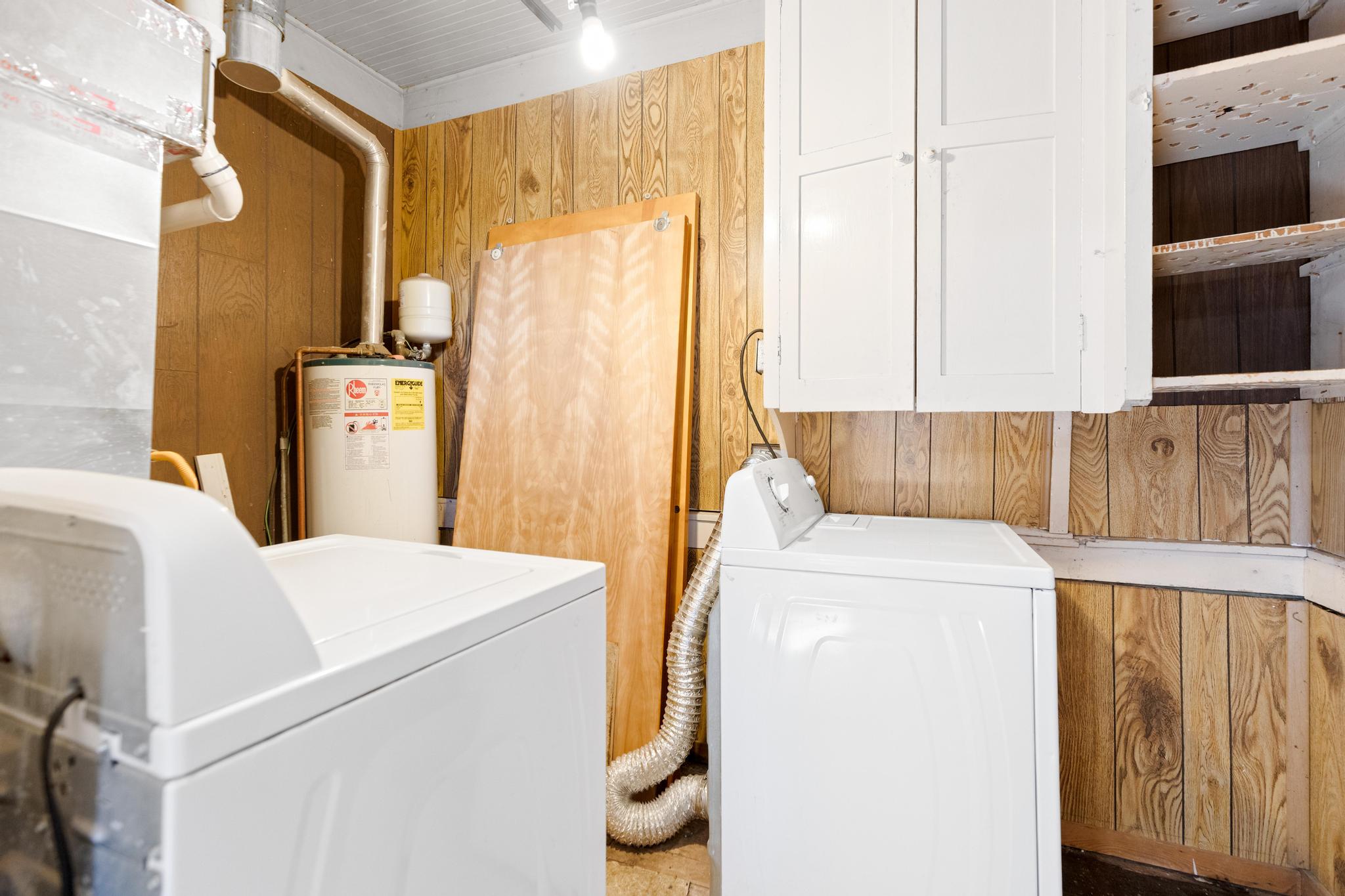 Washroom featuring separate washer and dryer, wood walls, cabinet space, and gas water heater