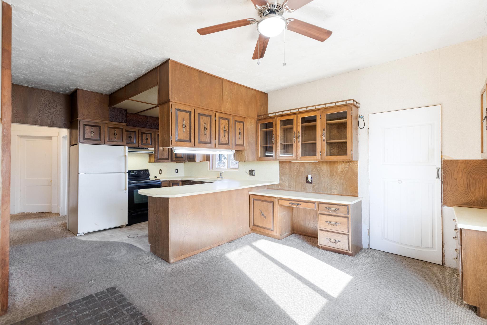 Kitchen with light countertops, black range with electric stovetop, freestanding refrigerator, a peninsula, and glass insert cabinets