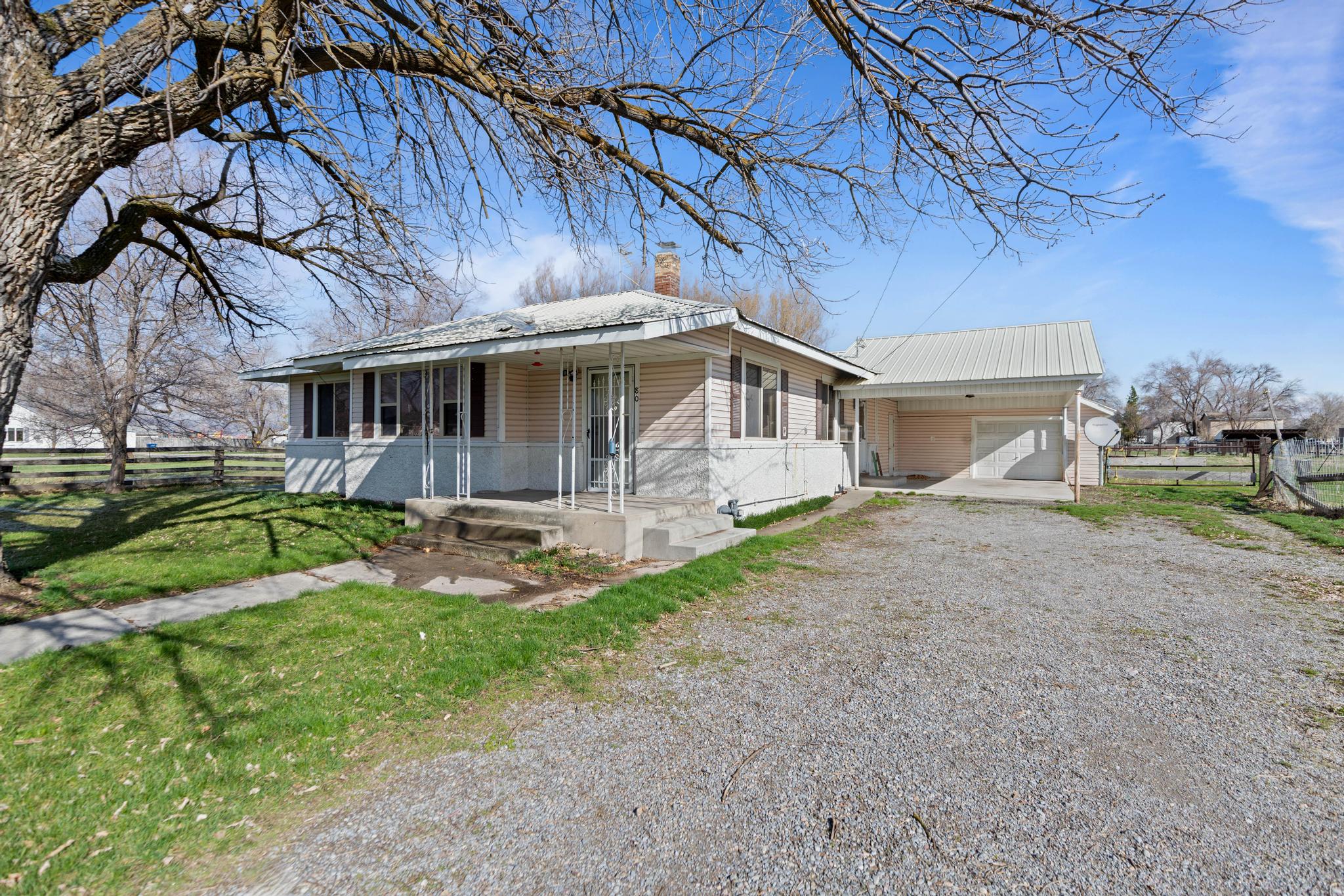 View of front of property with covered porch, gravel driveway, a front yard, and fence