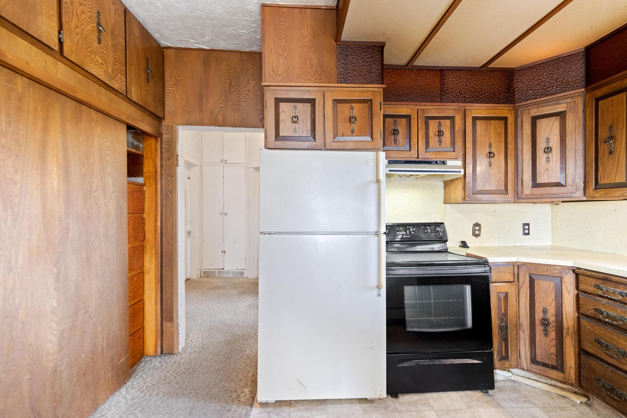 Kitchen featuring light countertops, freestanding refrigerator, brown cabinetry, under cabinet range hood, and black / electric stove