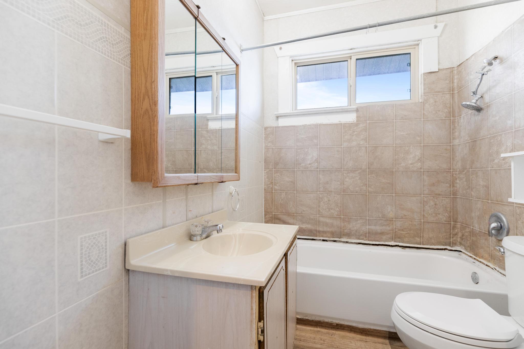 Full bathroom with tile walls, toilet, wood finished floors, vanity, and shower / washtub combination