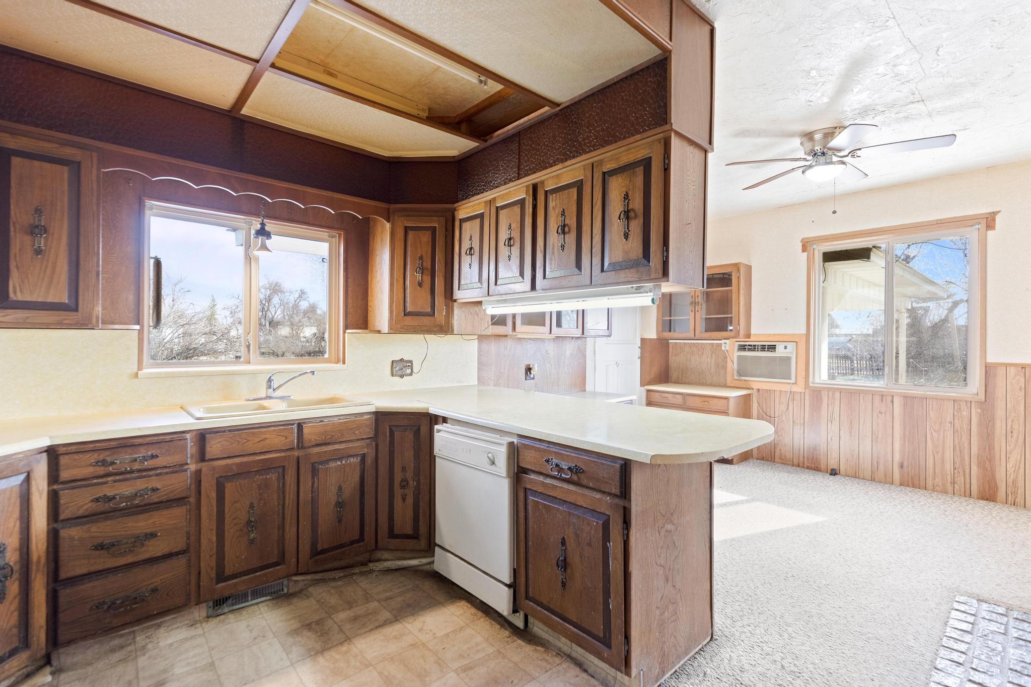 Kitchen featuring light countertops, a sink, a ceiling fan, wainscoting, and white dishwasher