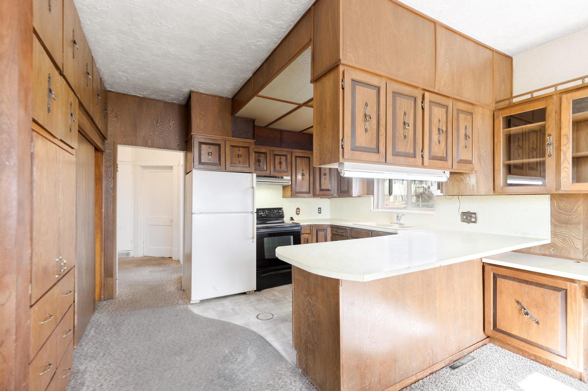 Kitchen featuring light countertops, freestanding refrigerator, a peninsula, under cabinet range hood, and electric range