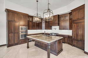 Kitchen featuring hanging light fixtures, glass insert cabinets, an inviting chandelier, an island with sink, and stainless steel appliances