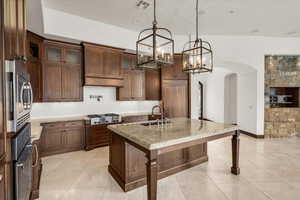 Kitchen featuring an inviting chandelier, light stone counters, stainless steel appliances, arched walkways, and a sink