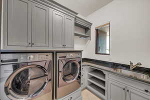 Clothes washing area featuring light tile patterned flooring, washing machine and clothes dryer, a sink, and cabinet space