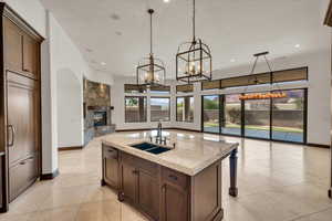 Kitchen with an inviting chandelier, a sink, open floor plan, a stone fireplace, and light stone countertops