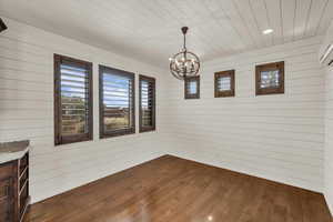 Unfurnished dining area featuring a chandelier, wooden walls, dark wood-style floors, and wood ceiling