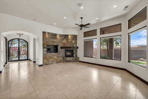Unfurnished living room featuring arched walkways, a ceiling fan, visible vents, a stone fireplace, and baseboards