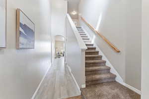 Stairway with arched walkways, wood finished floors, baseboards, and a towering ceiling