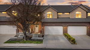 View of front facade with roof with shingles, driveway, stucco siding, and brick siding