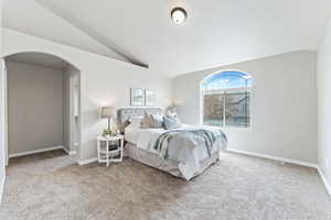 Carpeted bedroom with baseboards, arched walkways, vaulted ceiling, and a textured ceiling