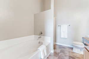 Bathroom with toilet, a bath, vanity, and baseboards