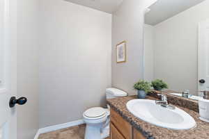 Half bathroom with toilet, vanity, and baseboards