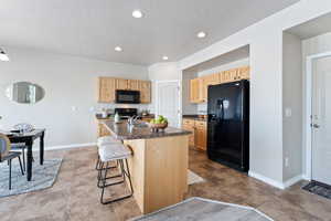 Kitchen featuring light brown cabinetry, black appliances, a breakfast bar, a sink, and dark countertops