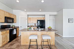 Kitchen featuring a breakfast bar, light brown cabinets, black appliances, and dark countertops