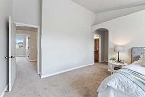 Bedroom featuring arched walkways, high vaulted ceiling, baseboards, and carpet floors