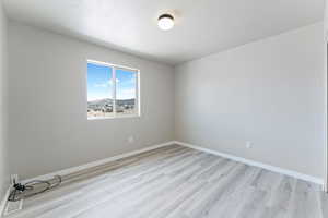Unfurnished room with a textured ceiling, light wood finished floors, and baseboards