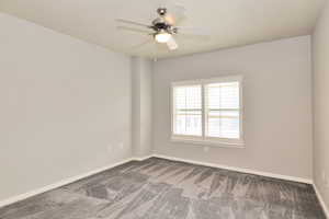 Unfurnished room with dark carpet, baseboards, and a ceiling fan