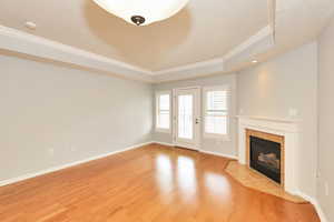 Unfurnished living room featuring baseboards, light wood-type flooring, a fireplace, crown molding, and a tray ceiling