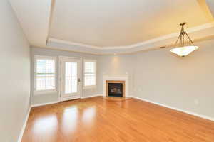 Unfurnished living room featuring a tray ceiling, light wood-type flooring, baseboards, and visible vents