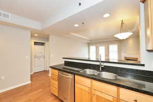 Kitchen with visible vents, a raised ceiling, a sink, light wood-type flooring, and stacked washer / dryer
