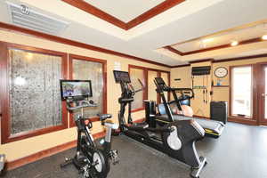 Workout room with a tray ceiling, baseboards, ornamental molding, and visible vents