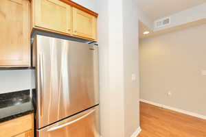 Kitchen with dark stone countertops, baseboards, light brown cabinets, freestanding refrigerator, and light wood-style flooring