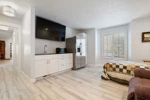 Bedroom with a sink, light wood-type flooring, stainless steel refrigerator with ice dispenser, and a textured ceiling