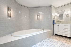 Primary Bathroom featuring a relaxing tiled tub, vanity, tile patterned flooring, and tile walls