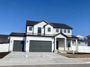 Modern farmhouse style home featuring concrete driveway, a garage, a standing seam roof, metal roof, and fence