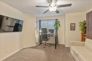 Carpeted office space with a textured ceiling, ceiling fan, and baseboards